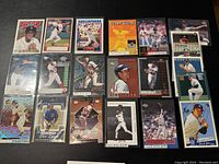 Photo showing assortment of 20 old baseball cards laid out on black surface, showing full fronts of cards with player photos and designs.