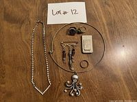 Image of assorted costume jewelry including necklaces, earrings, rings, brooch, and a small box laid on a wooden surface.