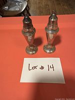 Pair of antique sterling silver salt and pepper shakers displayed on an orange tablecloth with handwritten Lot #14 card in front.