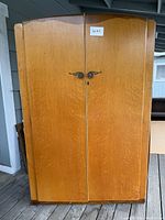 Front view of the vintage light wood armoire showing two doors with metal handles.
