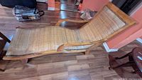 Side view of the bamboo lounge chair showing curved armrest and woven bamboo seat with wooden frame on laminate flooring.
