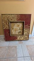 Oil painting with white flowers in a detailed decorative frame in red and beige tones.