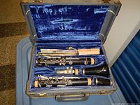 Open clarinet case showing disassembled clarinet pieces, mouthpiece, barrel and bell inside blue velvet lined compartments.