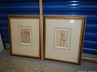 Two framed prints of delicate pink roses with stems, each approximately 19x16 inches, resting against a blue metal background with measuring ruler indicating size.