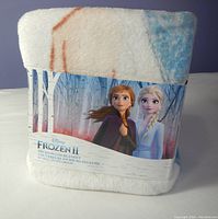 Folded Disney Frozen II microplush blanket in original packaging showing Anna and Elsa artwork and labeling.