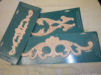 Three hardwood decorative appliques mounted on dark green cards, showing detailed floral and scroll carvings.