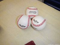 Three new Rawlings Official League baseballs with visible logos and red stitching placed on fabric surface.