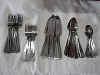 Image showing all pieces of the flatware set arranged in groups: large forks, dessert forks, cutting utensils, spoons, and teaspoons, displayed on a white textured surface.
