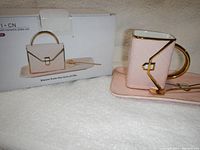 Photo of the tea and saucer set with box, showing packaging and mug shaped like handbag with gold handle and details.