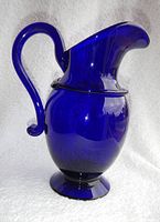Front and side view of vintage cobalt blue glass vase shaped like a pitcher with handle and flared spout.
