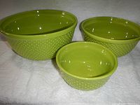 Three green nesting mixing bowls with hobnail exterior texture shown separately on white cloth background