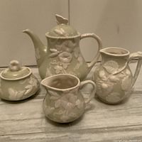Four-piece ceramic tea set including teapot, sugar bowl, creamer, and jug, pale green with white raised floral design