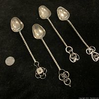 Four vintage spoons laid out on dark fabric showing the heart-shaped bowls and twisted handles ending in intricate filigree designs.