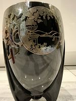 Front view of the black glass vase showing one circular silver overlay scenery with floral designs.