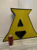 Front view of large yellow acrylic vintage uppercase letter A sign with black edges, showing size beside a can.