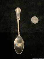 Full view of the sterling silver spoon alongside a quarter coin for size comparison, placed on a black textured background.