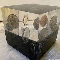 Close-up of the lucite cube showing embedded coins inside with reflective surfaces.