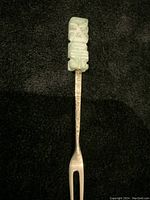 Top-down view of the vintage sterling silver cocktail fork with carved stone totem handle on a black background.
