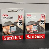 Two sealed packs of SanDisk Ultra 64GB SDXC UHS-I cards showing front packaging with camera image and speed markings.