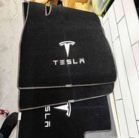 Close-up of the black carpet floor mats showing white Tesla logo embroidery with the text TESLA.