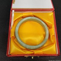 Solid light green jade bangle bracelet inside yellow satin-lined red jewelry box.