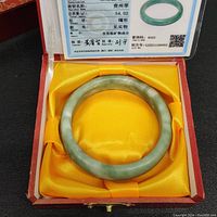 Green jade bracelet in a yellow satin-lined red jewelry box with certification card.