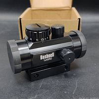 Side angle view of the Bushnell 1x40RD reflex dot sight on a black surface with open box behind.