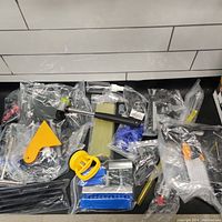 Overview of assorted dent removal tools laid out on black surface including yellow suction puller, glue sticks, blue tampers, spray bottles, metal tools, and other accessories mostly in plastic bags.