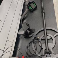 Side view showing the digital metal detector with armrest, adjustable stem, large round search coil, and connecting wire for headphones.