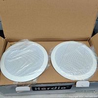 Two white circular 5.25 inch ceiling/in wall speakers with protective metal grill, packed in cardboard box, plastic wrapped.