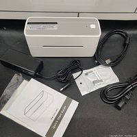 Phomemo PM-241-BT thermal label printer with power adapter and cables laid out on a surface with label rolls and manual.