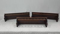 Three Ethan Allen antique dark solid pine Old Tavern wall shelves with spindle railing displayed together on white padded surface.