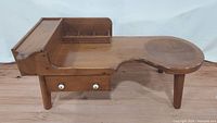Side view of antique cobbler's table showing drawer with white knobs and kidney-shaped top.
