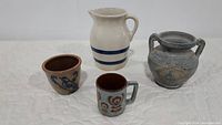 Four blue tone stoneware items: white pitcher with blue bands, two small pots and one mug.