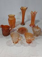 Collection of marigold carnival glass including multiple vases, cups, creamer, pitcher, and plate.