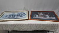 Both framed art prints placed horizontally against a white backdrop, displayed side by side on a quilted surface.