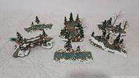 Six Dept 56 large decorative woodland village pieces arranged together on white fabric. Each piece detailed with snow, trees, logs, and water elements.