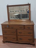 Front view of the dresser with mirror attached, showing drawer arrangement and brass handles.