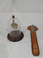 Wide view of both items: the pocket watch displayed under a glass dome with wooden base, and the leather sheathed letter opener.