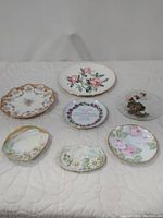 Seven assorted flowered plates displayed on a light-colored quilted surface