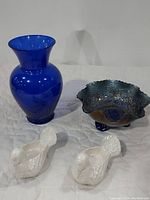 Cobalt blue glass flower vase, Fenton cobalt blue Carnival Glass bowl, and 2 white ceramic turkey salt cellars on a white surface.