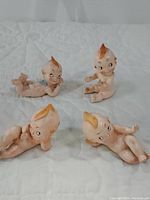 Overview of all four vintage Kewpie style porcelain baby figurines arranged on a white quilted surface.
