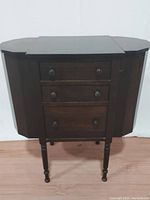 Front view of the antique walnut sewing cabinet showing three drawers and side storage compartments.
