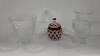 Three items on white background: Waterford ice bucket, ruby red covered sugar bowl, clear glass vase