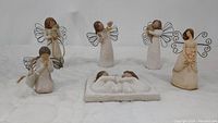 Seven Willow Tree angel and figurine pieces arranged on white fabric, showing wire wings and natural tones.