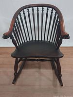Front view of Windsor style rocking chair showing dolphin head carved armrests and spindle backrest.