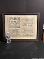 Framed 19th century broadsheet playbill advertising multiple theatrical performances at Nurney Theatre, leaning against a black background with a water bottle for scale.