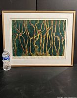 Full view of framed artwork with water bottle for size reference, showing green and gold abstract art print titled 'Autumn in Front'