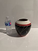 Full view of ceramic pot next to water bottle for size comparison showing red, white, black colors and geometric lines.