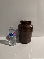 Brown glazed ceramic pot standing upright next to a 16.9 oz bottle of Pure Life water for scale.